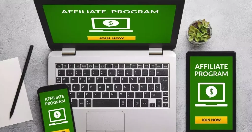 Laptop and smartphone displaying “Affiliate Program” with a green background and “Join Now” button, alongside a plant and notepad.