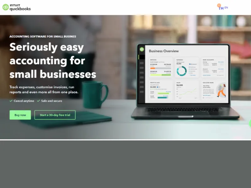A laptop displays QuickBooks accounting software, featuring a business overview dashboard, with a coffee mug and notebook nearby.