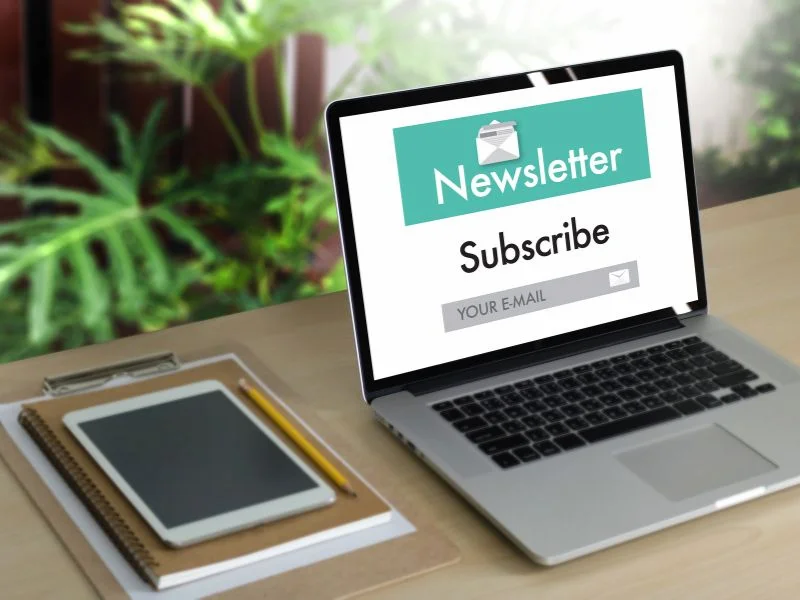 Laptop on desk showing a newsletter subscription form with 'Subscribe' button and email input field, surrounded by green plants, representing Freelance2Retire’s community engagement and email marketing efforts