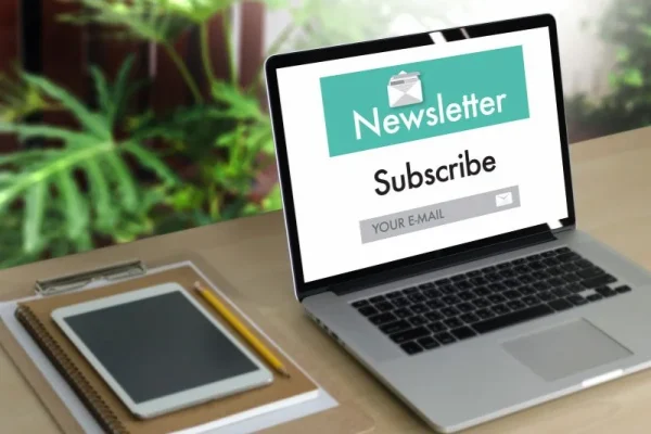 Laptop on desk showing a newsletter subscription form with 'Subscribe' button and email input field, surrounded by green plants, representing Freelance2Retire’s community engagement and email marketing efforts